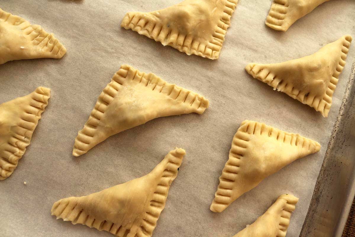 Puff pastry triangles with crimped edges, on a baking sheet ready for the oven.