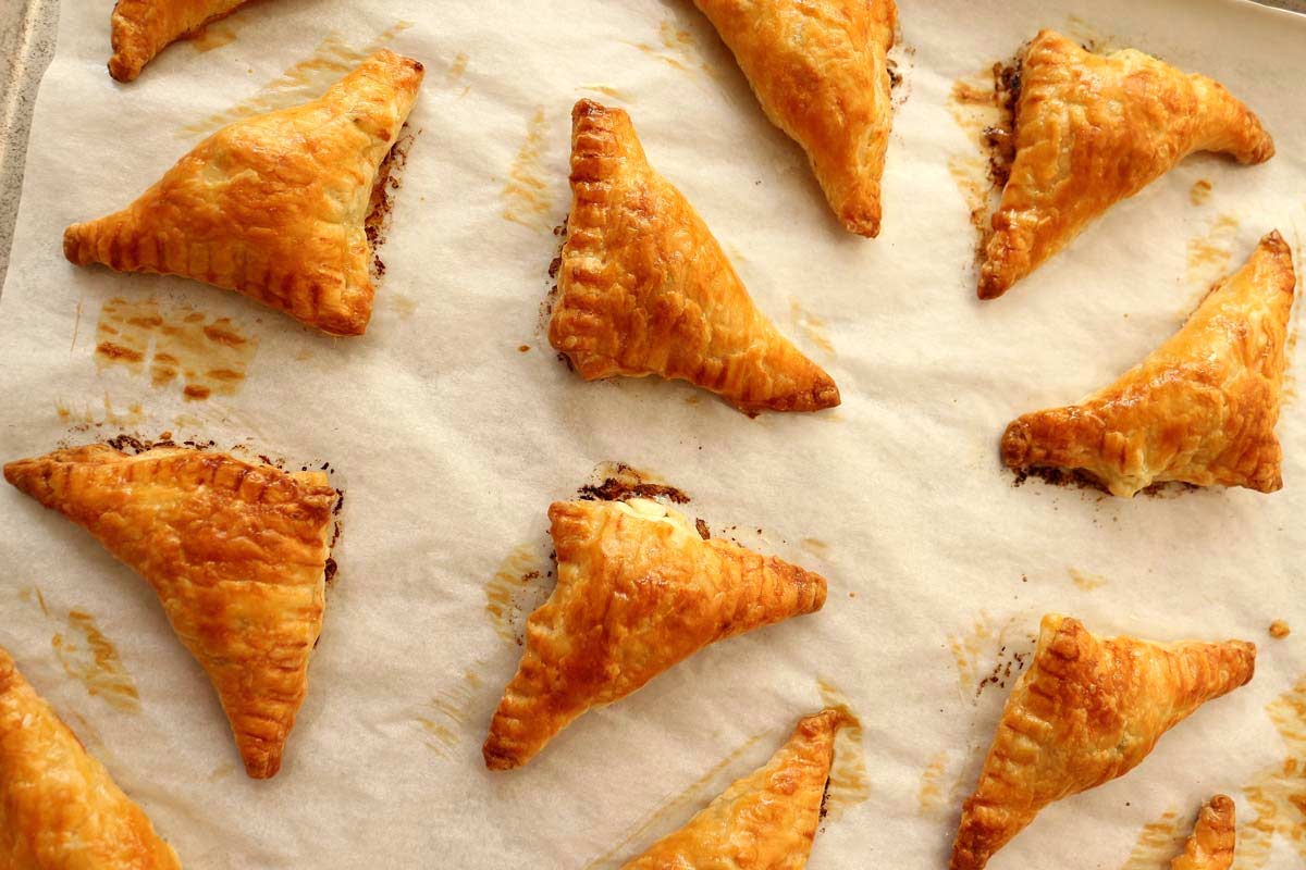 Golden brown cheese borek puff pastry triangles on a baking sheet.