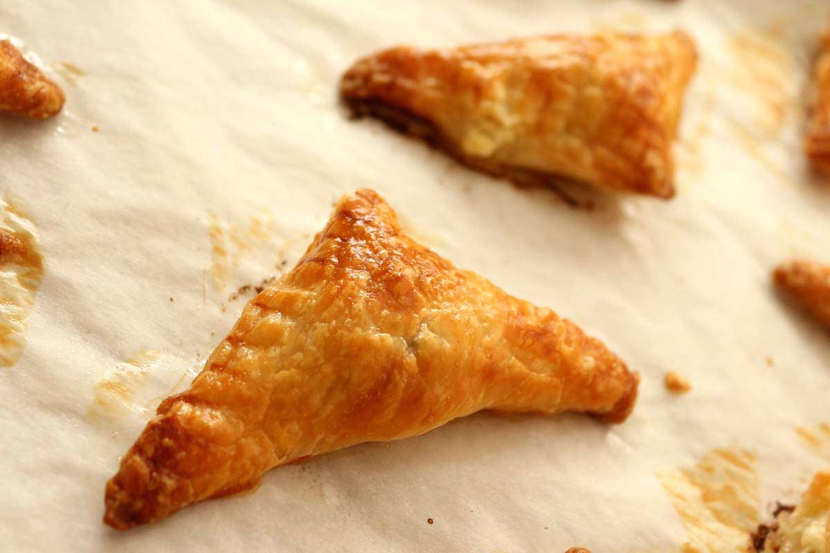 Closeup of a golden brown puff pastry triangle on a baking sheet.