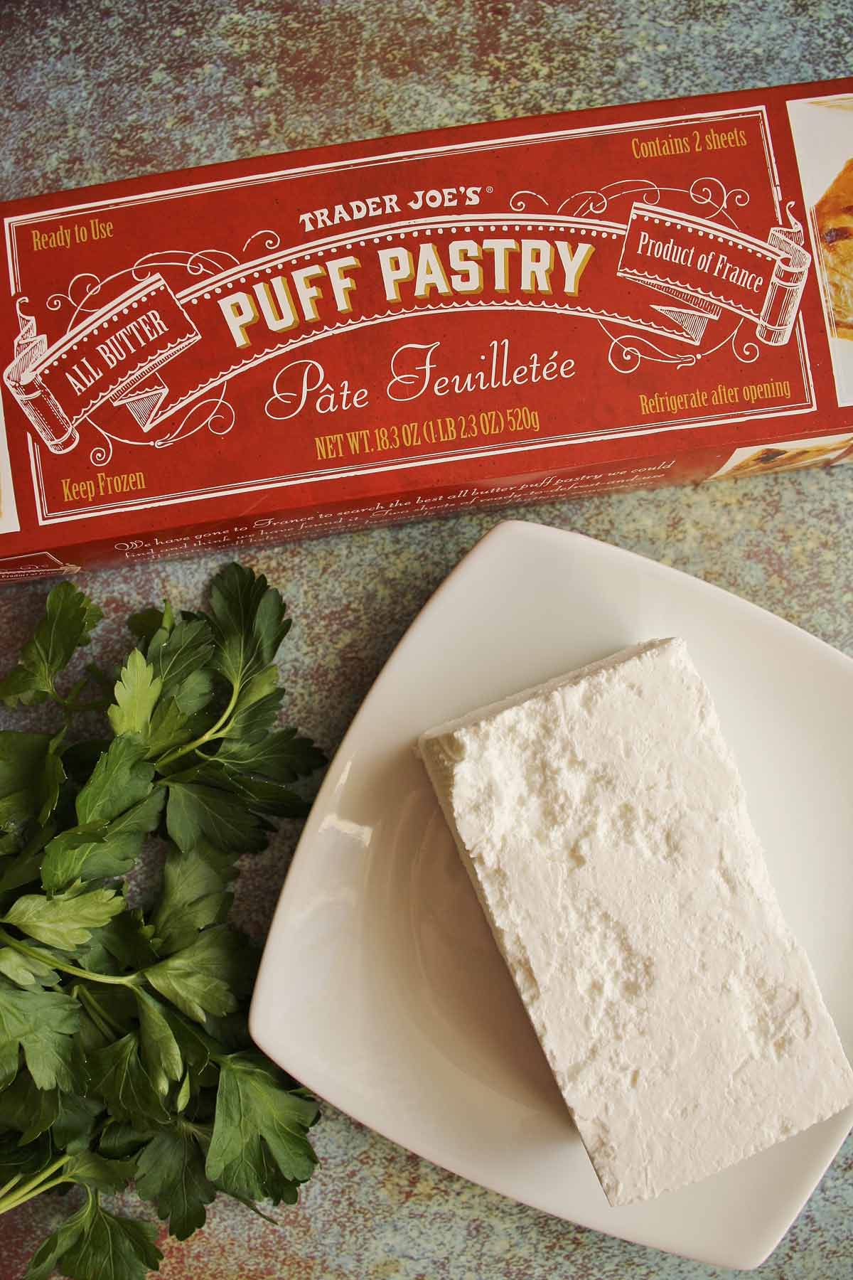 A package of Trader Joe's puff pastry, a block of feta cheese, and flat leaf parsley.