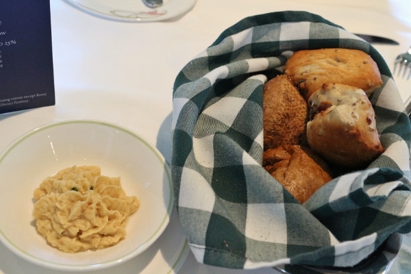 a basket of bread rolls next to a bowl of chickpea spread