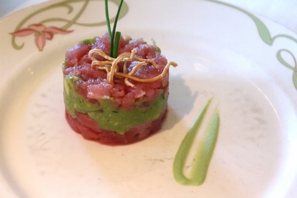 a layered cylinder of raw tuna and avocado on a white plate