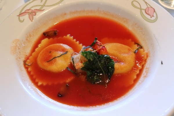 two raviolis in tomato broth topped with lobster meat