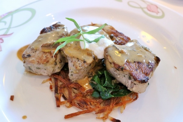 three pieces of seared pork served over a crispy potato pancake on a white plate