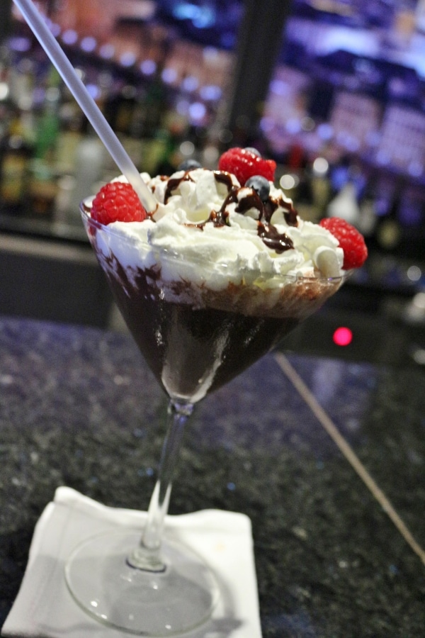 A glass of a cocktail glass with a chocolate drink topped with whipped cream and raspberries