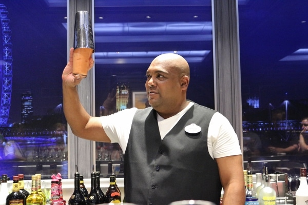 A man behind a bar holding up a cocktail shaker