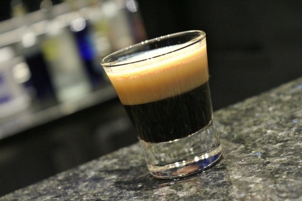 A closeup of a shot glass filled with a black drink with a foamy topping