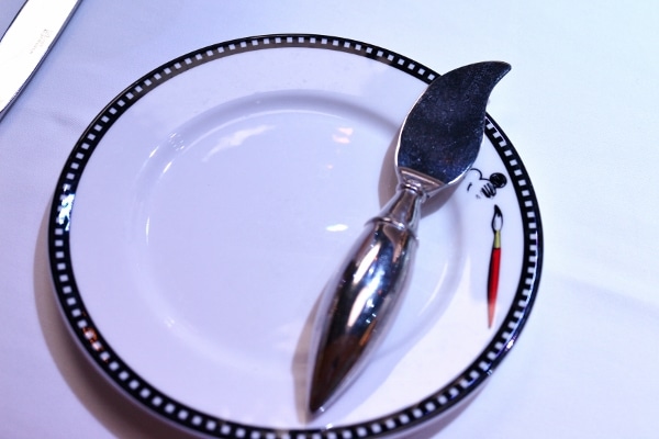 A close up of a plate with an artist palate shaped metal spreader on one side