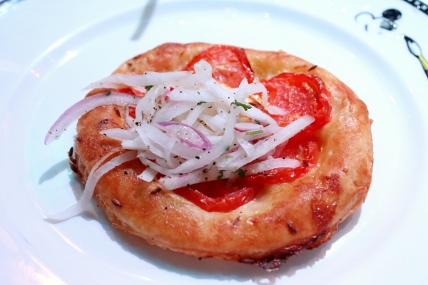 A closeup of a round flatbread topped with tomato slices and red onion