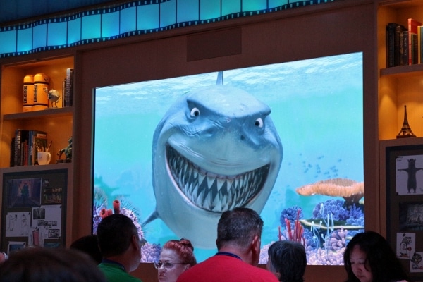 Bruce from Finding Nemo smiling with his big sharp teeth at a group of people