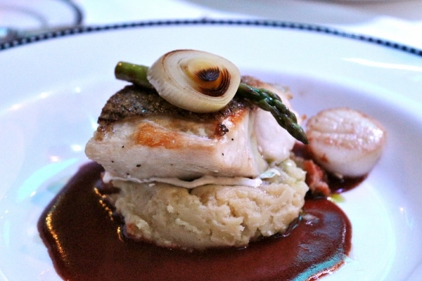 A piece fish over a scoop of mashed potatoes and dark brown sauce on a plate