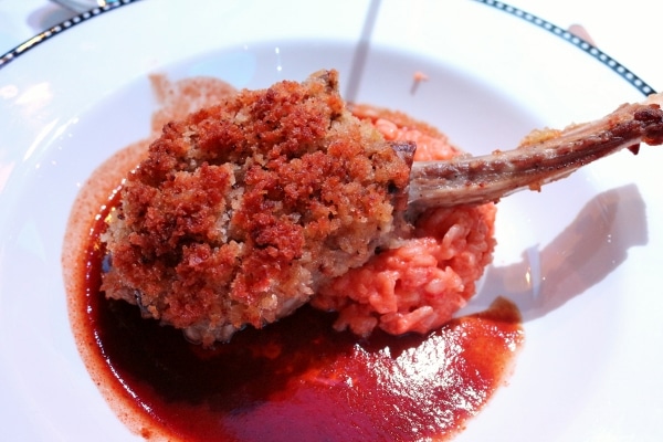 A piece of breaded meat on a bone over red risotto and dark brown sauce