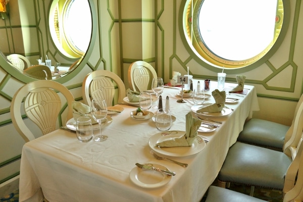 a long dining table with pale green wall decorations and a porthole window behind it