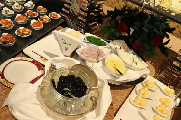 a glass dish of black caviar with various accompaniments on a buffet