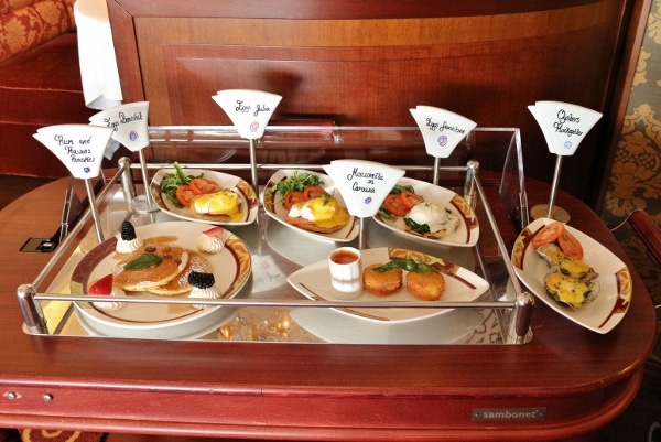 a rolling cart of plates of food with labels of what they are