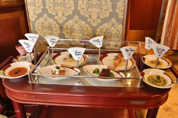 another rolling cart of plates of food with labels of what they are