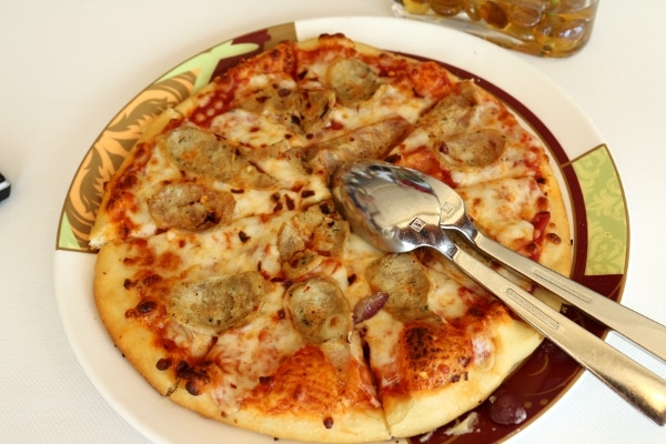 a pizza topped with sliced sausage and silverware for serving
