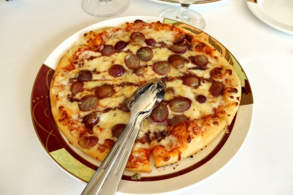 A pizza topped with halved grapes and silverware for serving