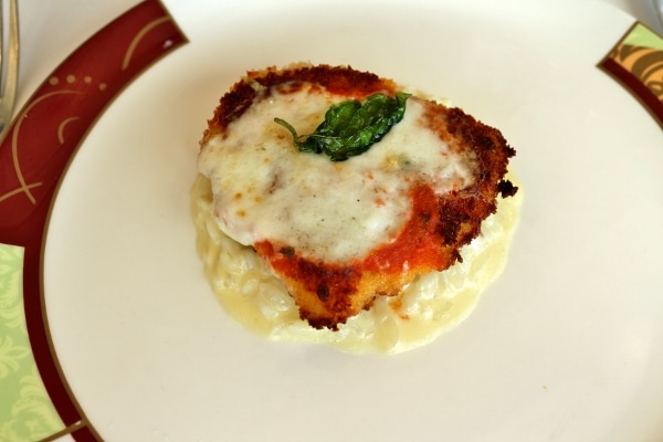A piece of crispy chicken parmesan topped with cheese and a basil leaf