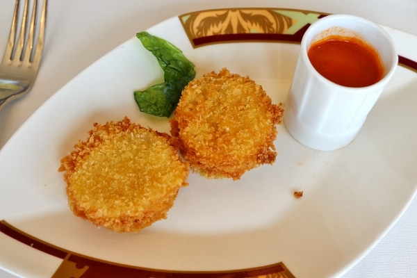 two crispy pieces of fried cheese with a container of tomato sauce for dipping
