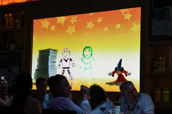 a screen with animated drawings next to Sorcerer Mickey
