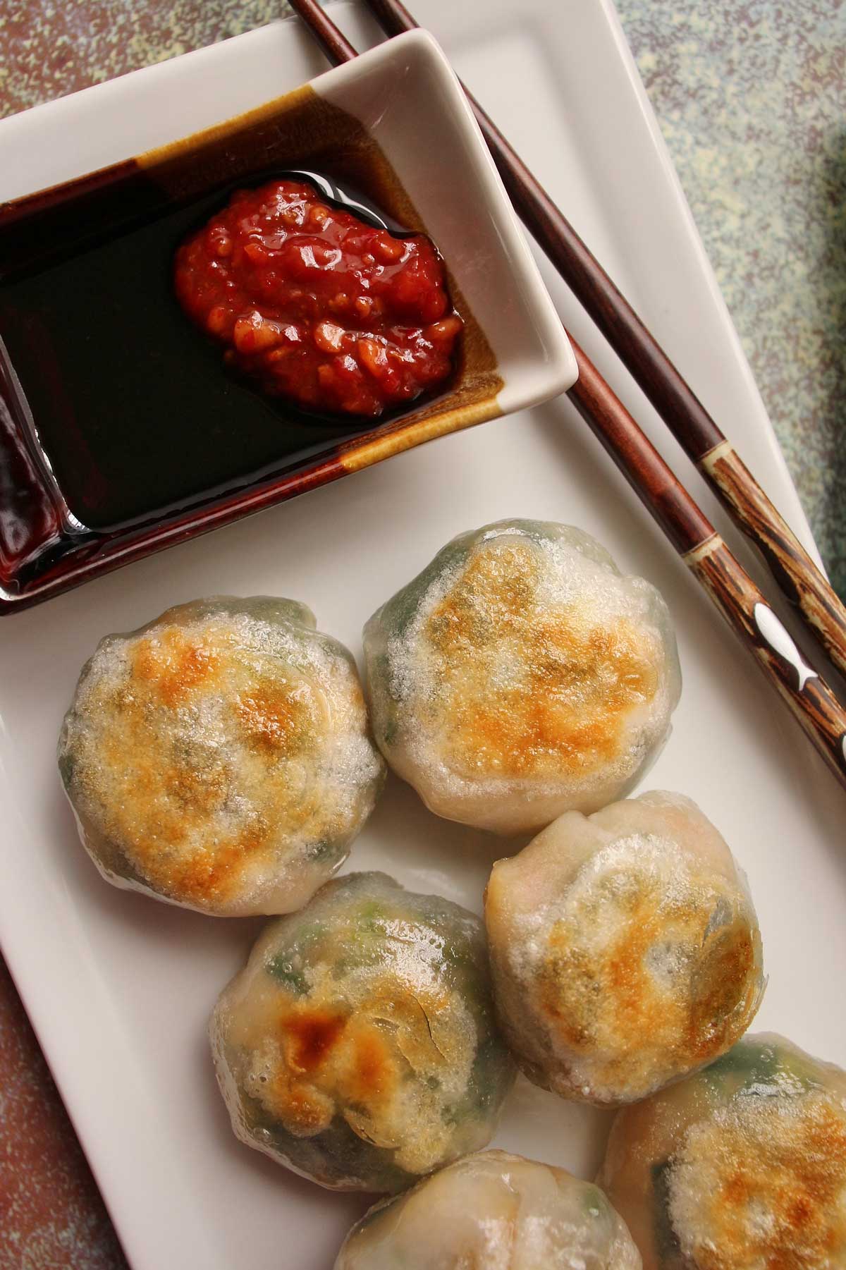 Closeup of pan-fried chive dumplings on a white rectangular plate with dipping sauce.