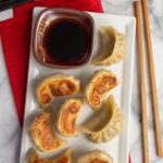 Mushroom dumplings on a white rectangular dish with a bowl of dipping sauce on the side.
