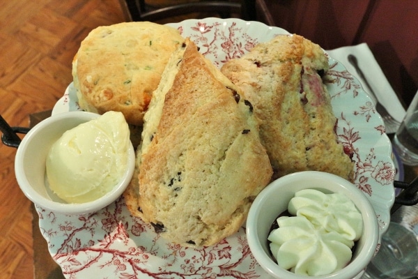 a plate of three scones with small cups of butter and cream