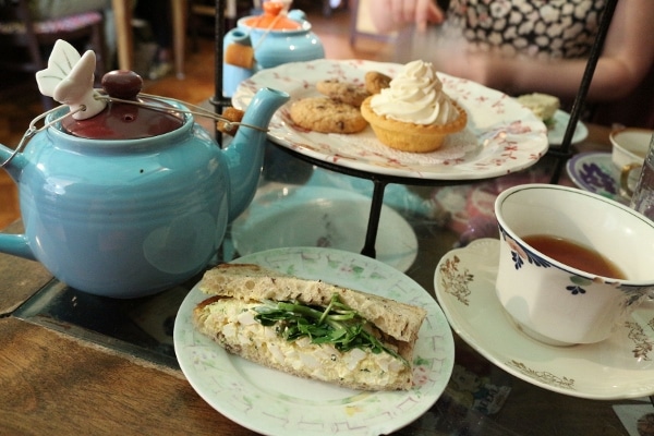 a sandwich on a plate next to a blue teapot and white teacup filled with tea