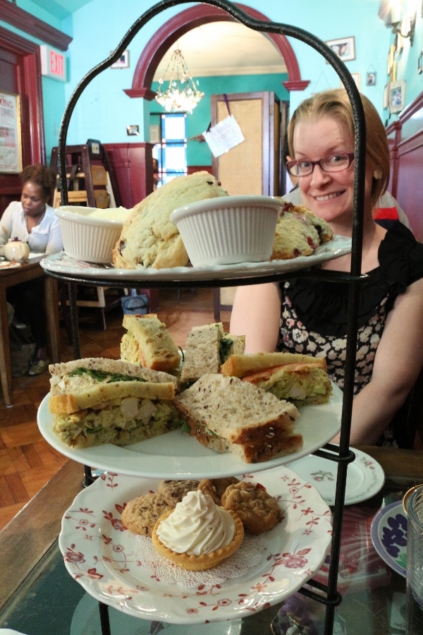 a three-tiered afternoon tea display of food with a woman on the other side