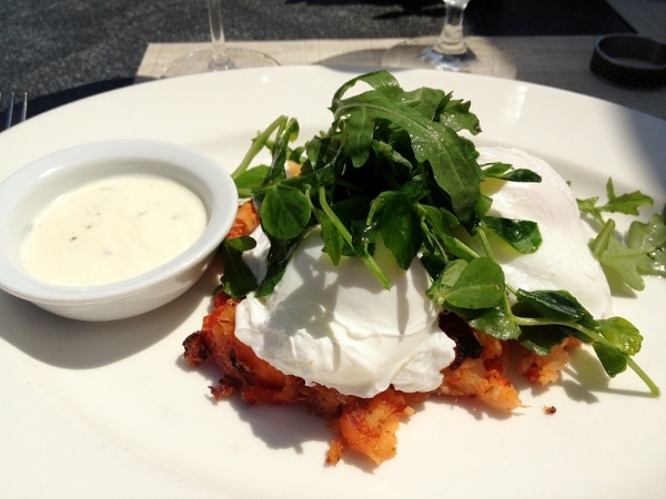 poached eggs topped with greens served over lobster hash on a white plate