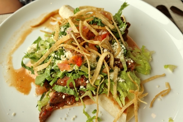 A plate of food topped with shredded lettuce, tomatoes, and crispy tortilla strips