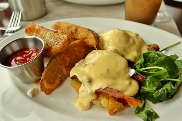 a plate of Eggs Benedict made with fried green tomatoes, served with fried potato wedges