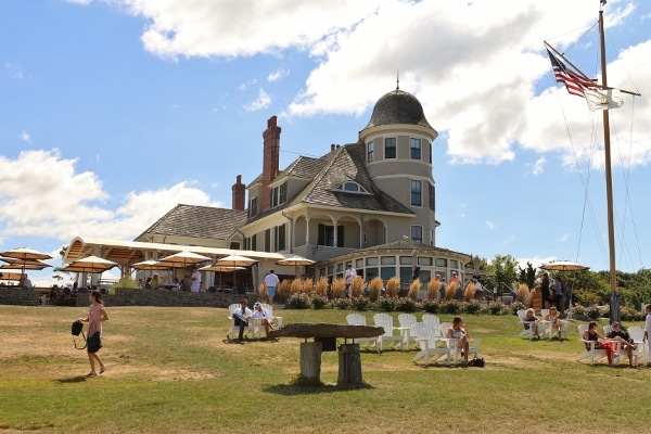 a small and elegant looking inn with a large lawn and Adirondack chairs in front