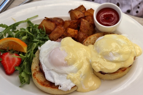 A plate of Eggs Benedict with home fries and salad on the side