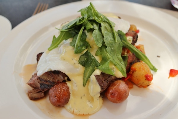 steak and baby potatoes topped with eggs, bearnaise sauce, and greens on a white plate