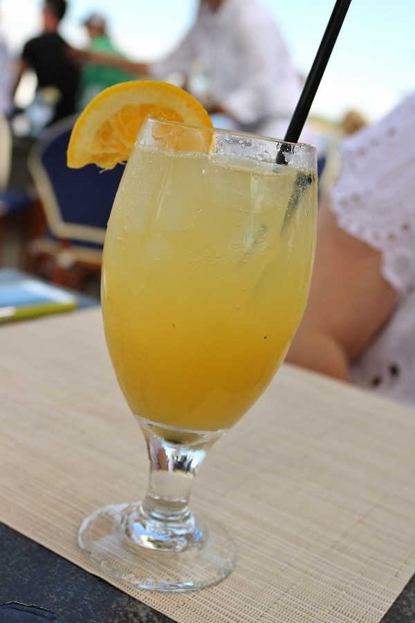 a goblet filled with a light orange drink with an orange slice garnish