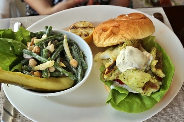 a bean salad in a bowl next to a fish sandwich on a white plate