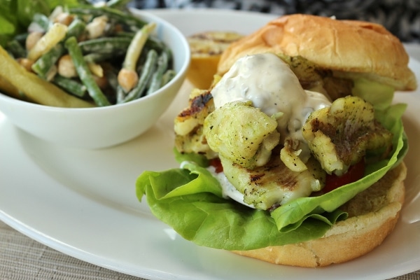 a closeup of a fish sandwich on a burger bun next to a bowl of beans