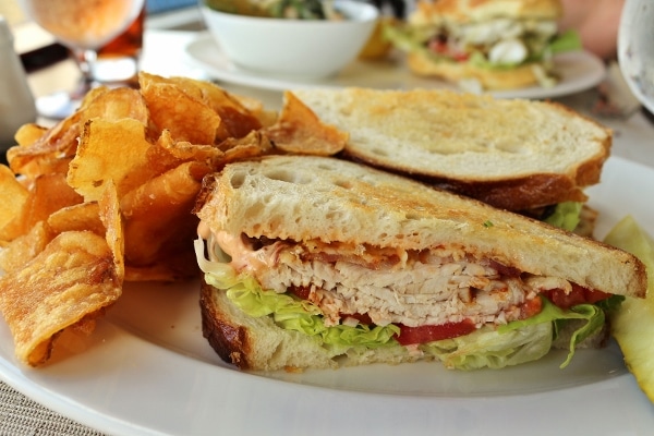 A closeup of a sandwich on a plate with potato chips on the side