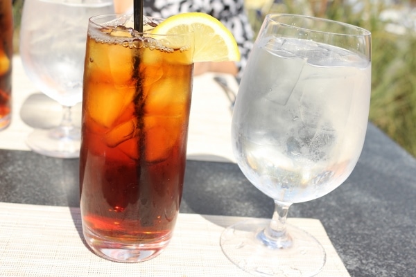 a tall glass of iced tea next to a glass goblet of water