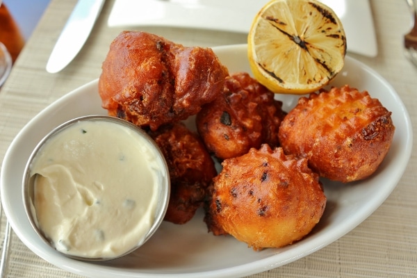 a platter with fried clam cakes, a cup of white dipping sauce, and grilled lemon half