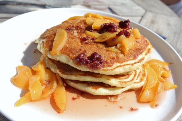 a stack of pancakes topped with fruit served on a white plate