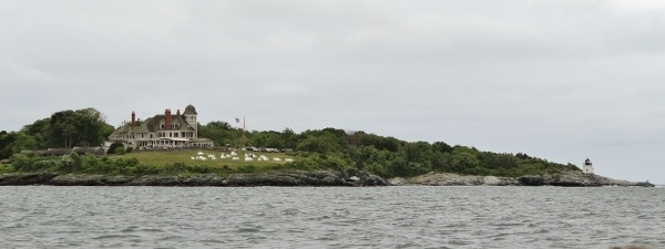 view from the water of a small seaside inn with a green lawn and Adirondack chairs