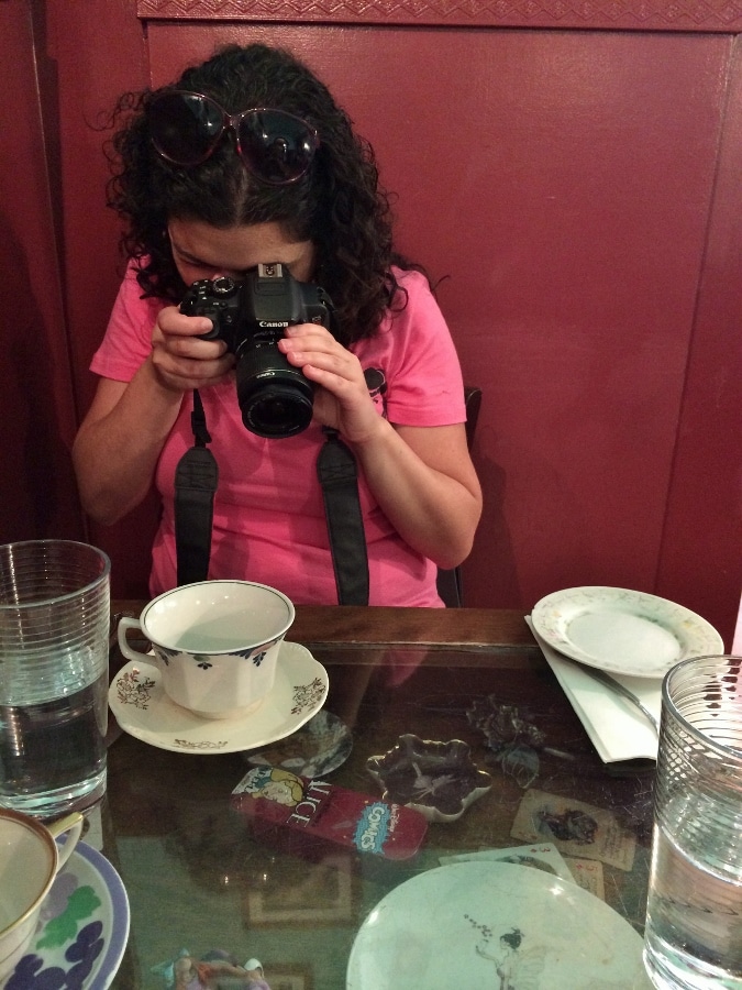 A woman taking a photo of a cup and saucer on a table