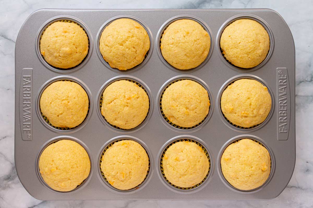 Corn muffins in a metal muffin pan on a marble surface.