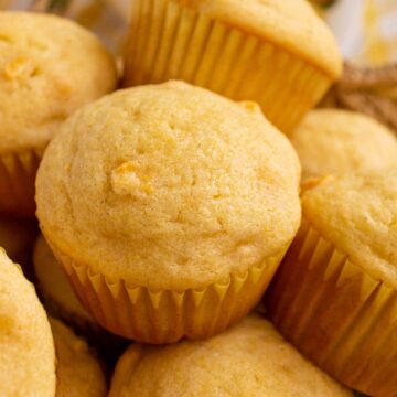 Closeup of standard sized corn muffins piled on top of each other in a basket.