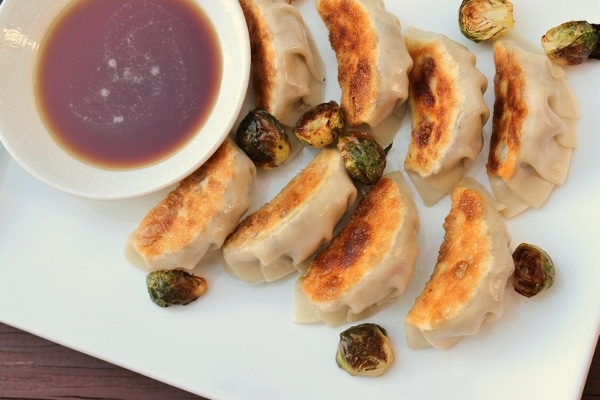 overhead view of pan-fried dumplings on a white plate scattered with roasted brussels sprouts