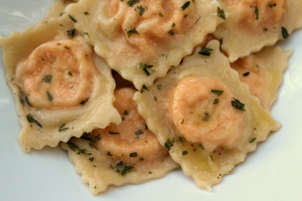 A closeup of carrot ravioli in herbed butter served in a white dish