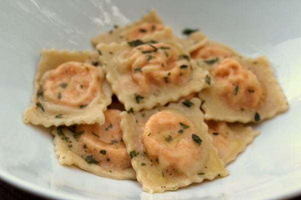 a shallow white bowl filled with ravioli tossed in a butter and herb sauce